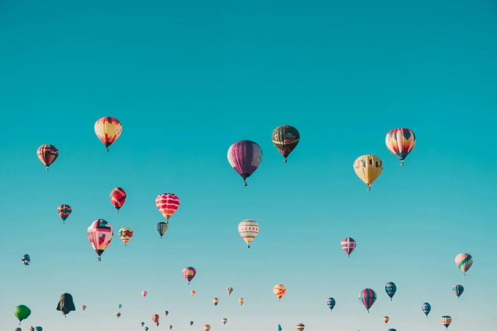 Envol de nombreuses montgolfières colorées dans un ciel bleu clair.
